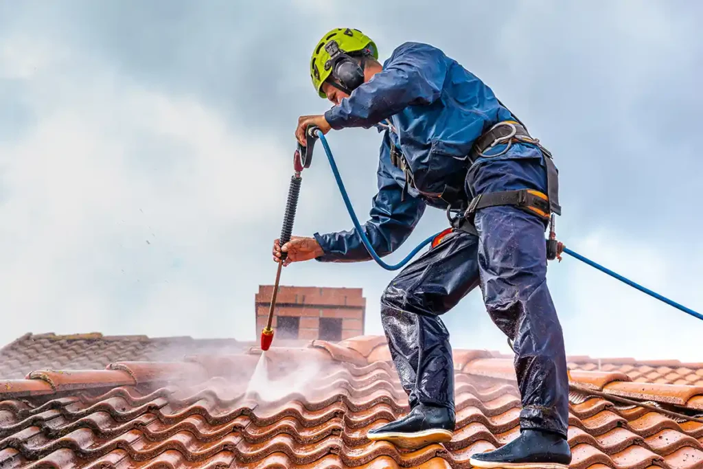 Das Foto zeigt einen Arbeiter, der auf einem Dach in Dieburg während der Reinigung arbeitet. Er trägt Schutzkleidung und verwendet spezielle Reinigungsgeräte, um das Dach von Verschmutzungen zu befreien.