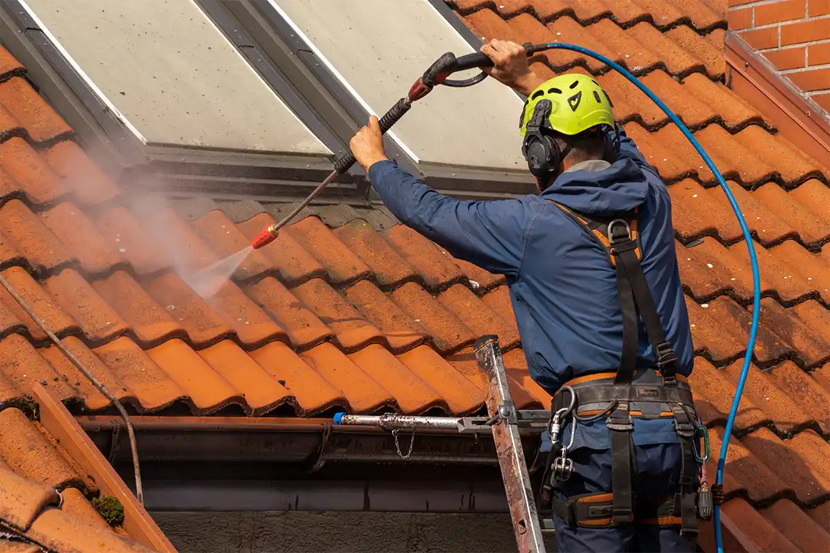 Das Bild zeigt einen Mitarbeiter, der während der Dachreinigung auf einem Dach in Groß-Zimmern arbeitet. Er trägt eine Schutzkleidung und ist dabei, mit professionellen Reinigungsgeräten und Werkzeugen das Dach von Ablagerungen zu befreien.